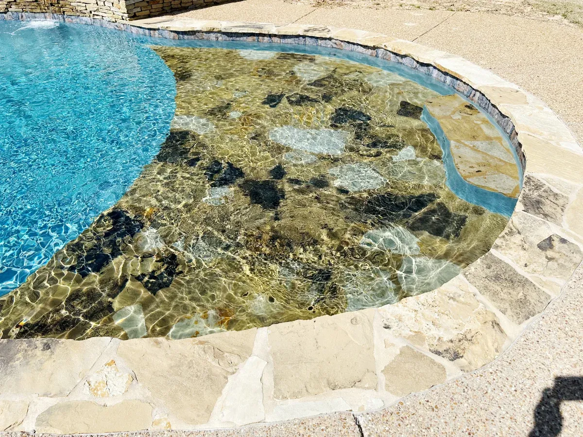 This swimming pool features a large stone step down area for shallow water access.